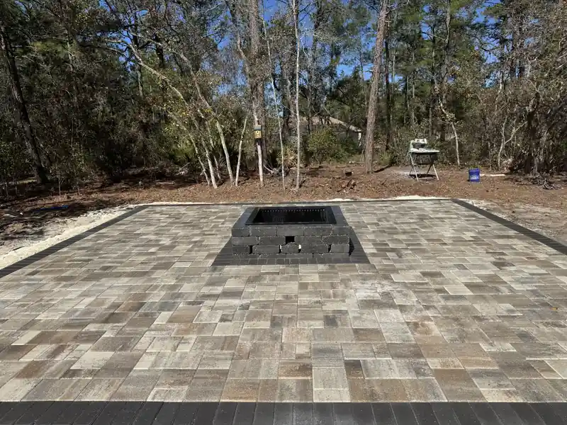 Paver patio with a square block fire pit and a charcoal border on a cleared wooded lot in Citrus Springs