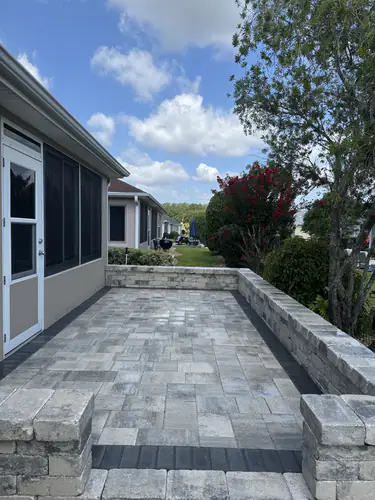 Narrow grey and white patio beside a screened room in The Villages, edged by a low capped wall and two pillars