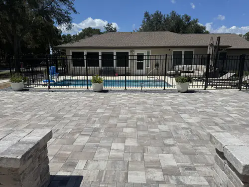 Paver walkway following the black pool fence into the patio with bare soil beds on either side