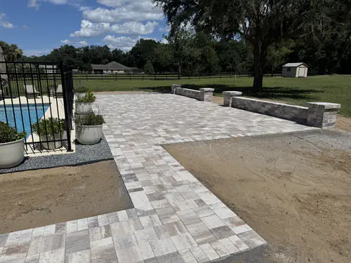 Backyard patio beside the fenced pool with potted plants on the pavers