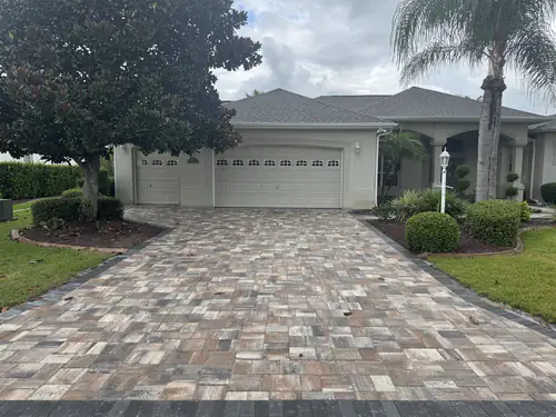 Front view of a two car garage in Ocala with a new tan, white and grey paver driveway and dark side borders