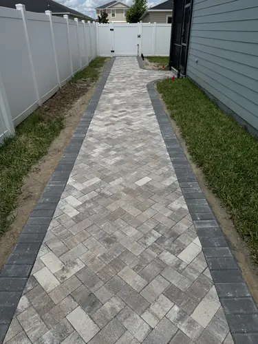 Side yard herringbone walkway with charcoal soldier course edges leading to a white fence gate