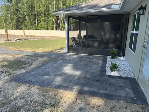Screened porch patio in charcoal pavers with a white rock bed at a new Ocala home
