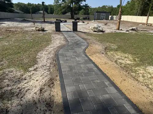 Dark bordered walkway winding toward block pillars and boulders in an Ocala yard