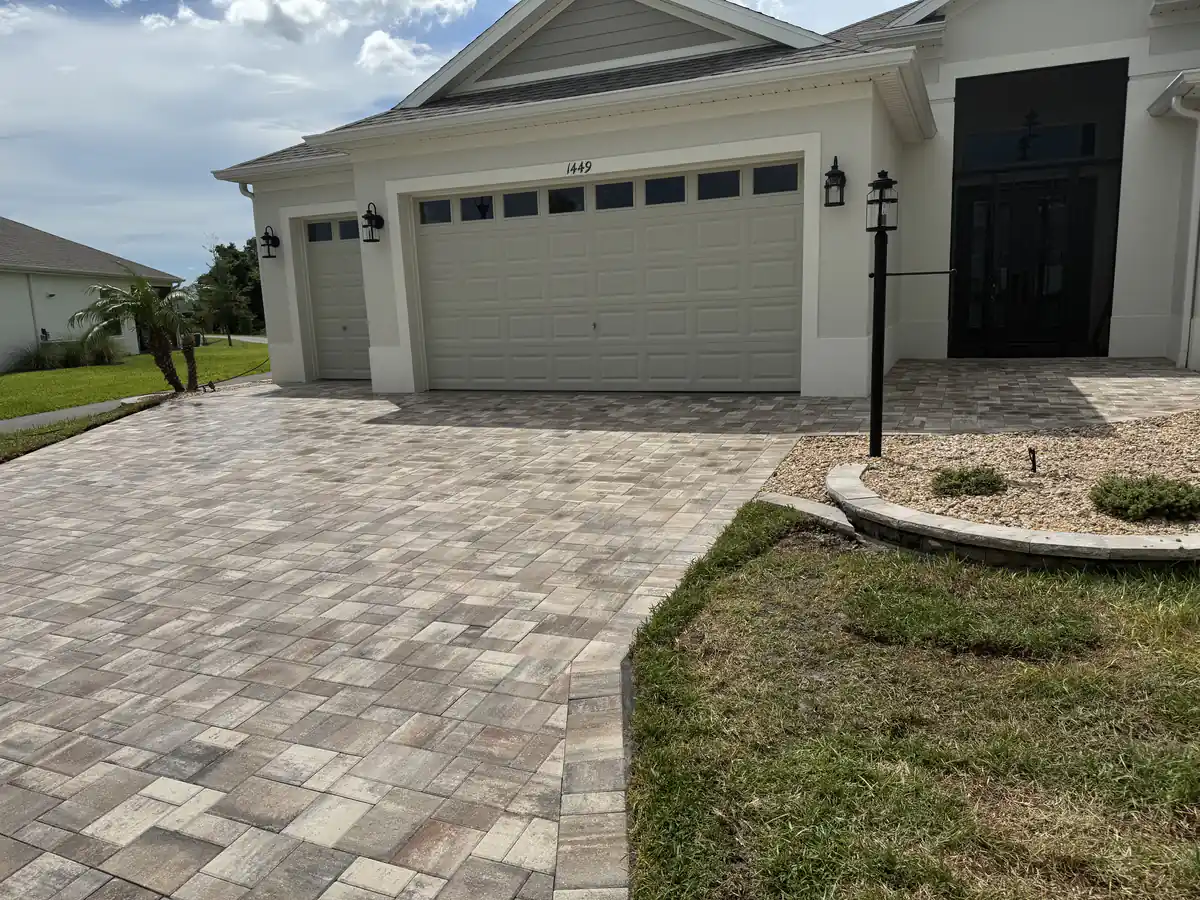 Angled view of a blended tan and grey paver driveway meeting the lawn and a curved rock bed in The Villages