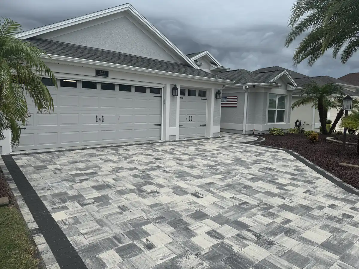 Angled view of a navy, grey and white paver driveway with a dark border in front of a white garage in The Villages