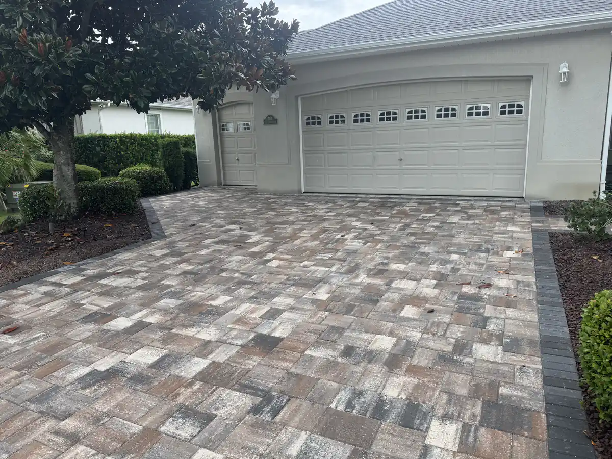 Tan and grey blended paver driveway with a charcoal edge curving past a magnolia tree at an Ocala stucco home