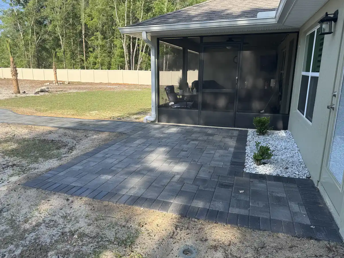 Screened porch patio in charcoal pavers with a white rock bed at a new Ocala home